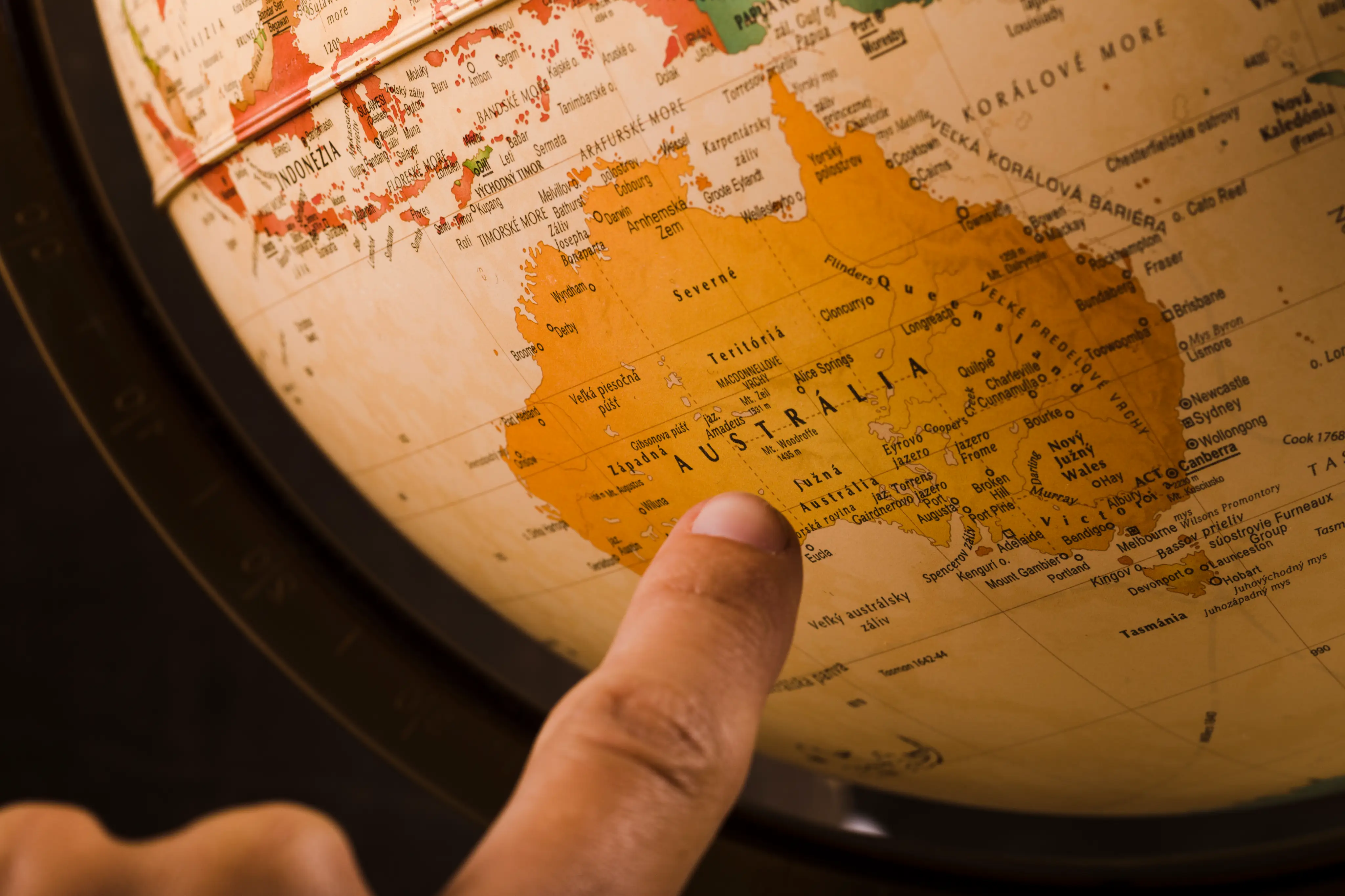 A hand pointing to Australia on a globe